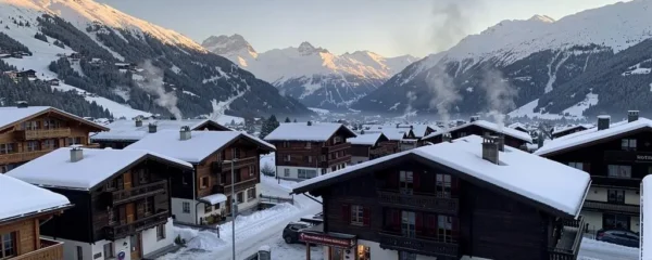 Traditional wooden chalets with carved balconies positioned on snowy Alpine slopes above Gstaad village, with mountain peaks visible under winter afternoon light